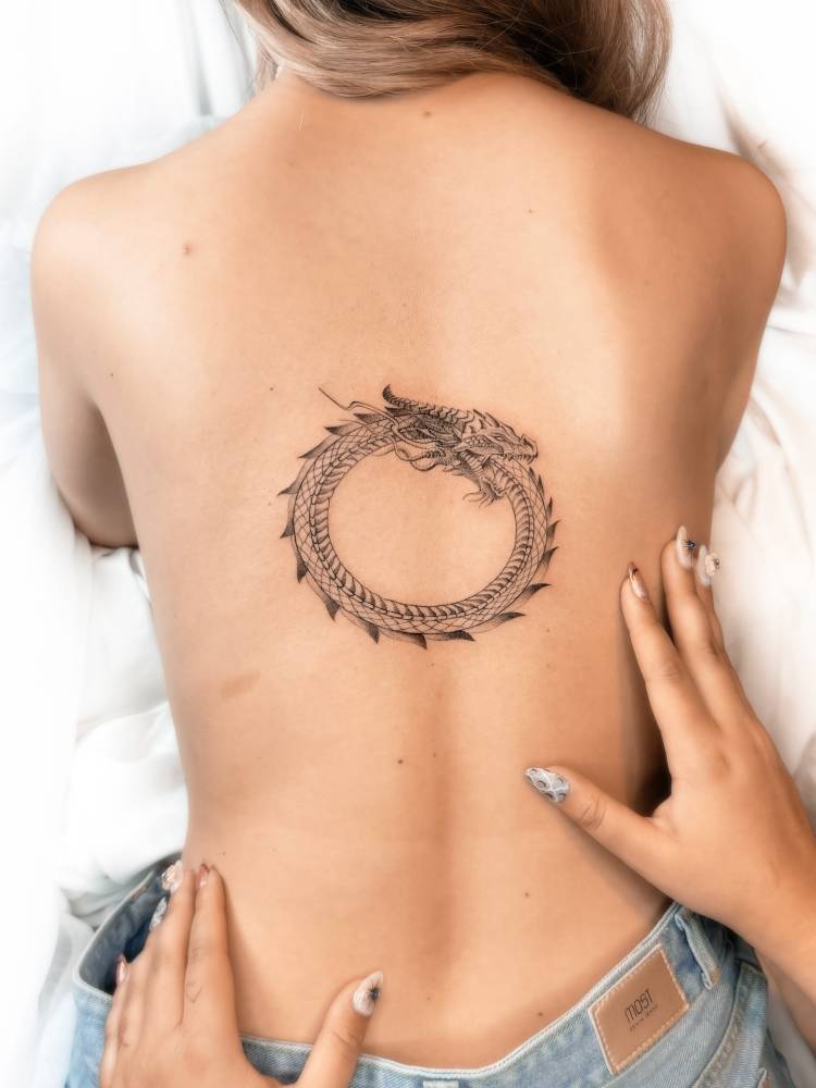 Dragon ouroboros tattoo in illustrative style located on the back.