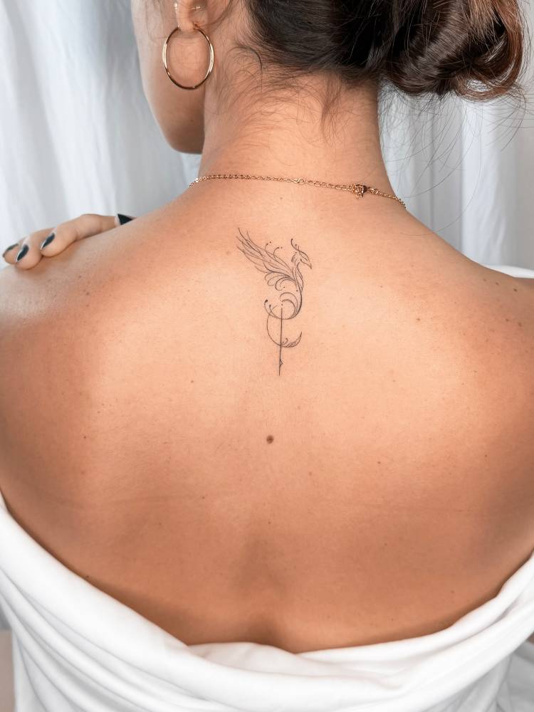 Phoenix tattoo in fine line style located on the upper back.