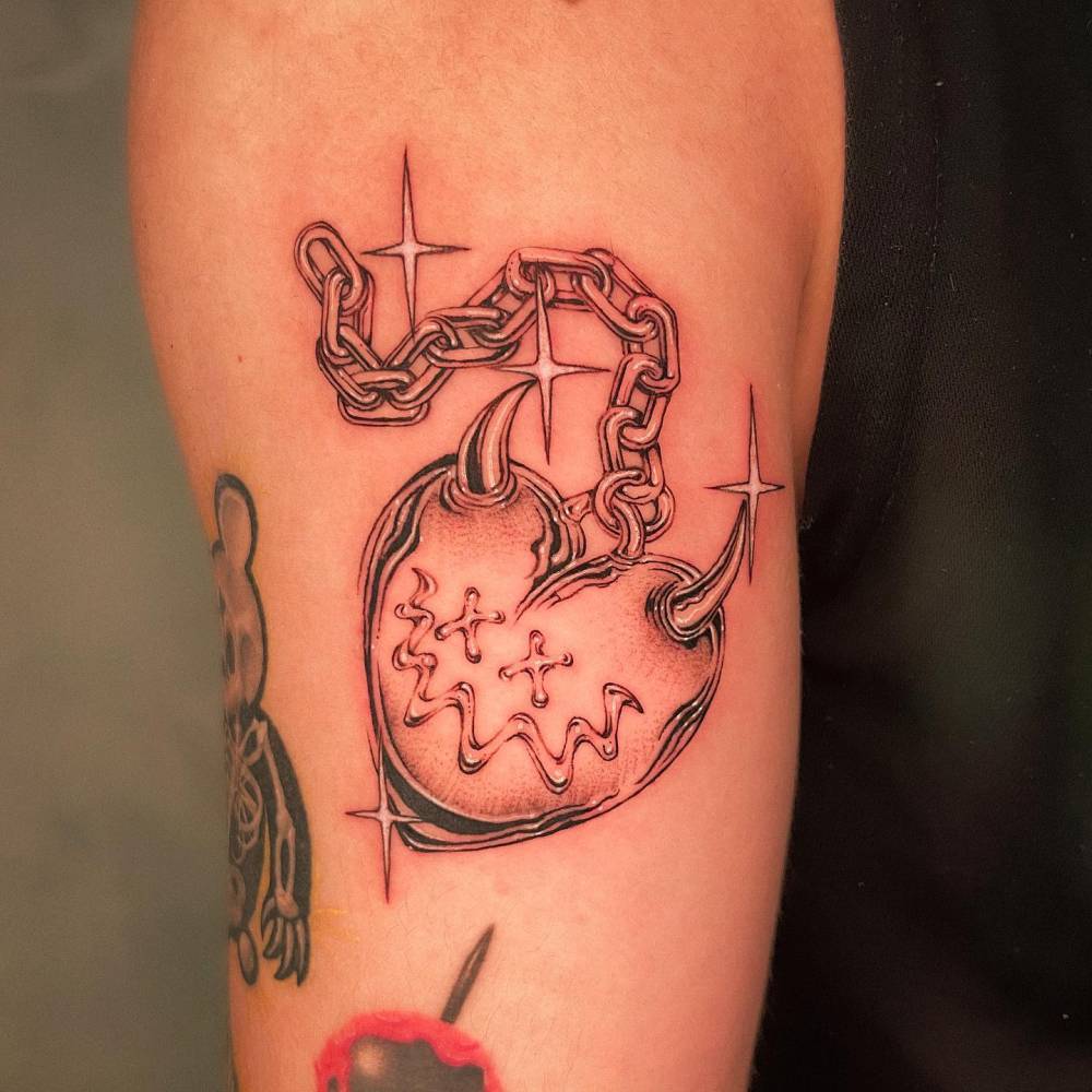 Illustrative style heart pendant tattoo located on the upper arm.