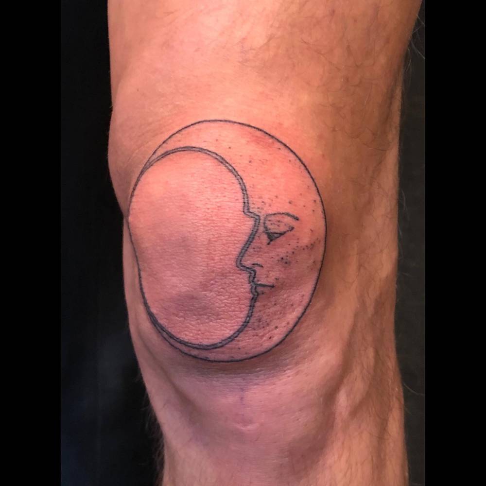Moon face tattoo in illustrative style located on the knee.