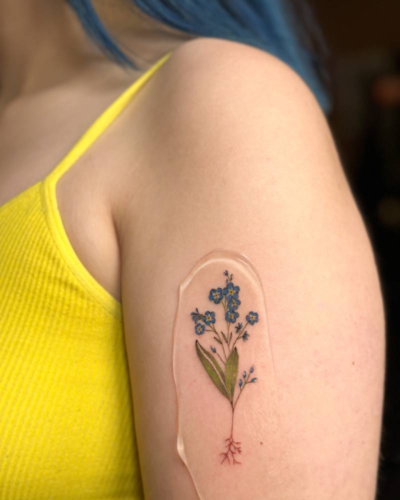 Illustrative style forget-me-not bouquet tattoo located on the upper arm.