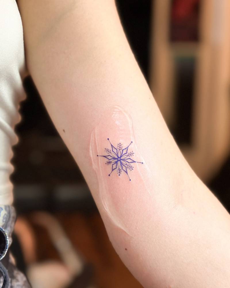 Purple snowflake tattoo located on the inner arm, fine line style.