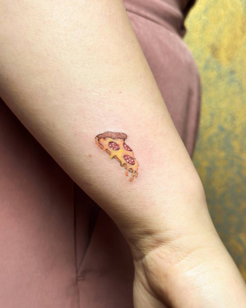 Tiny pepperoni pizza tattoo placed on the wrist, illustrative style.