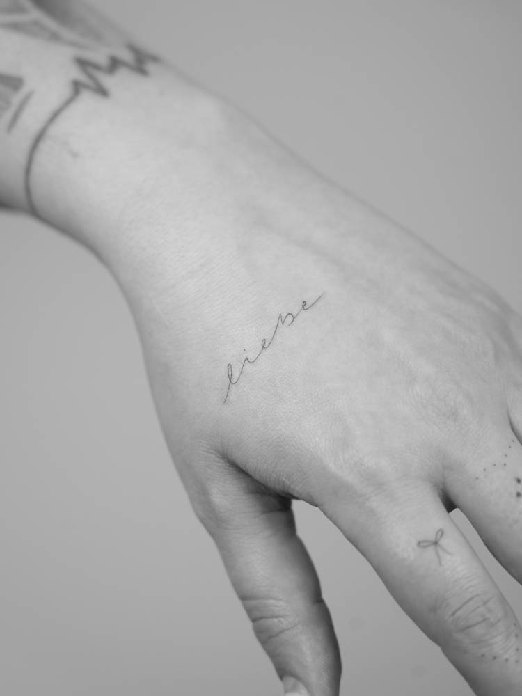 Handwritten font word "liebe" tattooed on the hand.