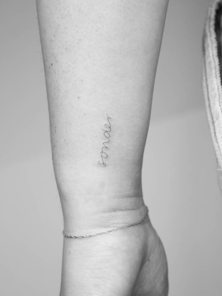 "Sonder" lettering tattoo in handwritten font placed on the wrist.