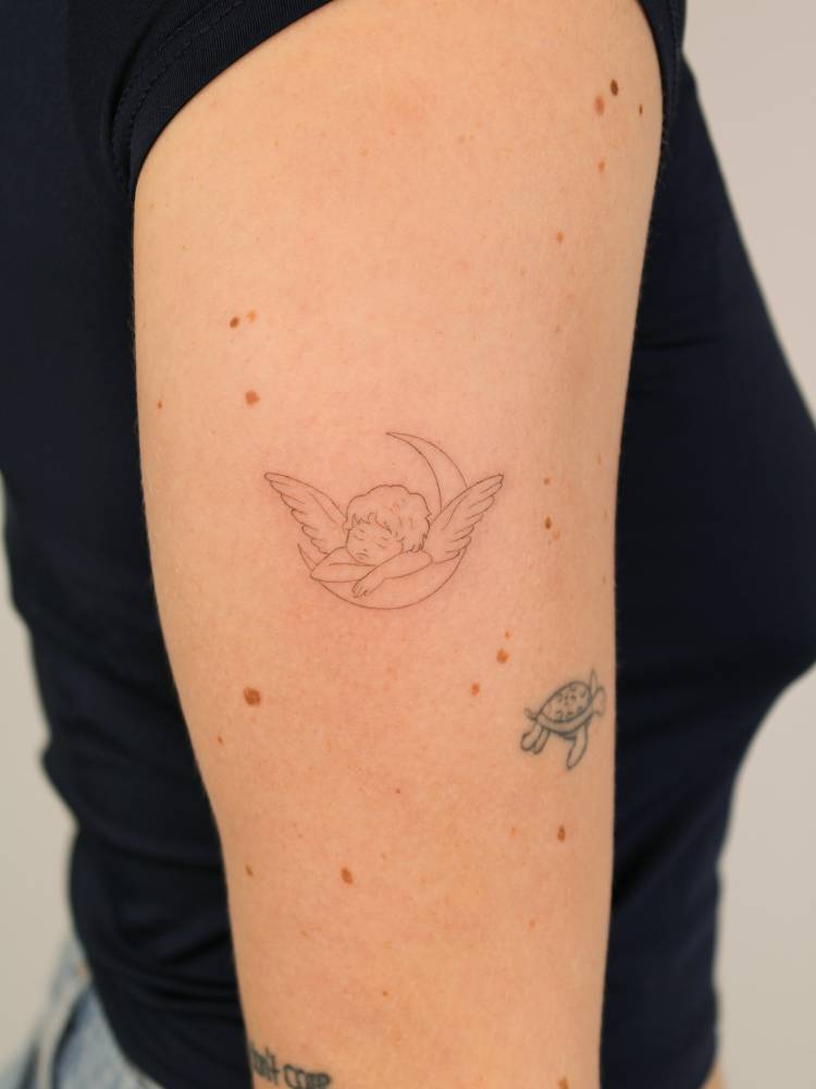 Fine line style sleeping cherub tattoo located on the upper arm.