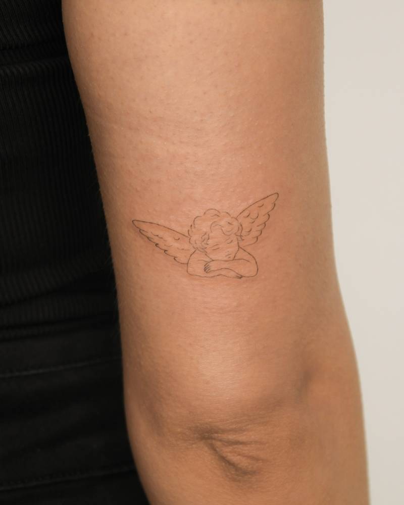 Sleeping cherub tattoo located on the tricep, done in fine line style.