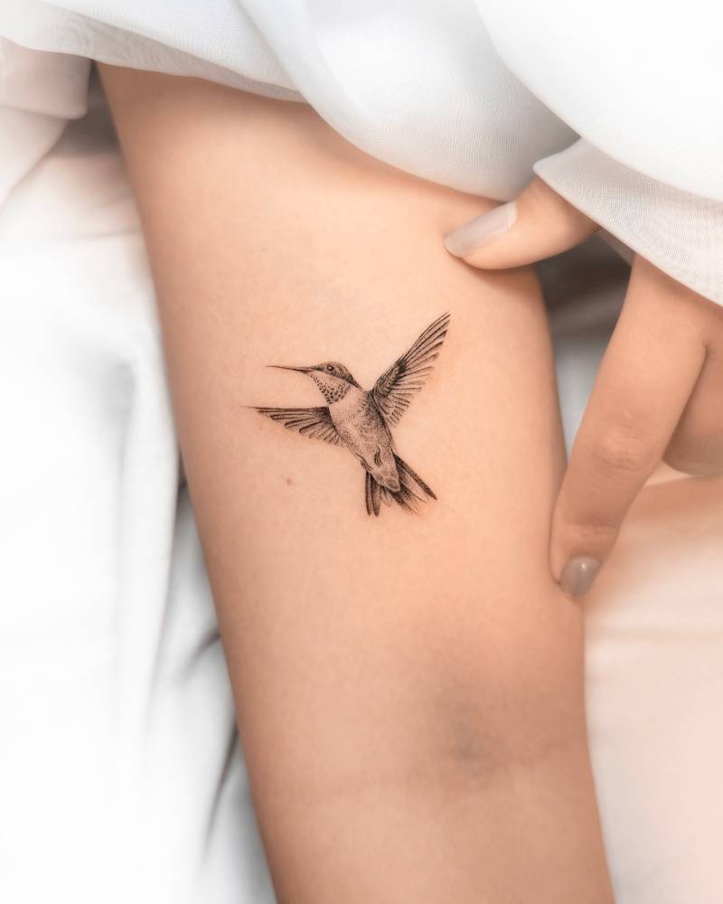 Little hummingbird tattoo in micro-realistic style placed on the bicep.