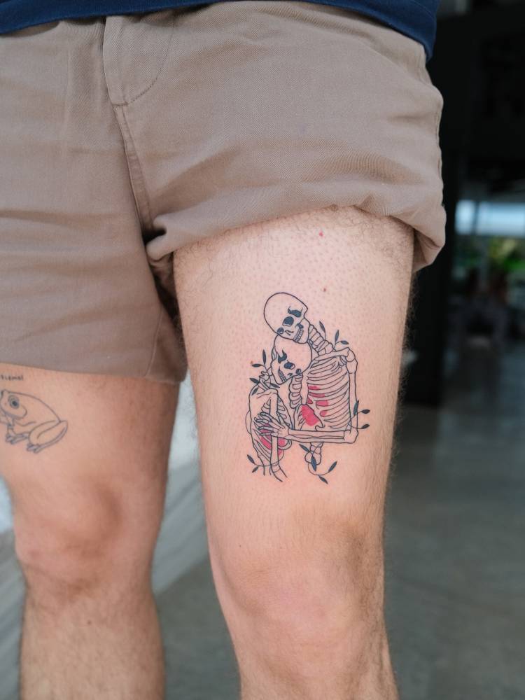 Illustrative style skeleton hug tattoo located on the thigh.