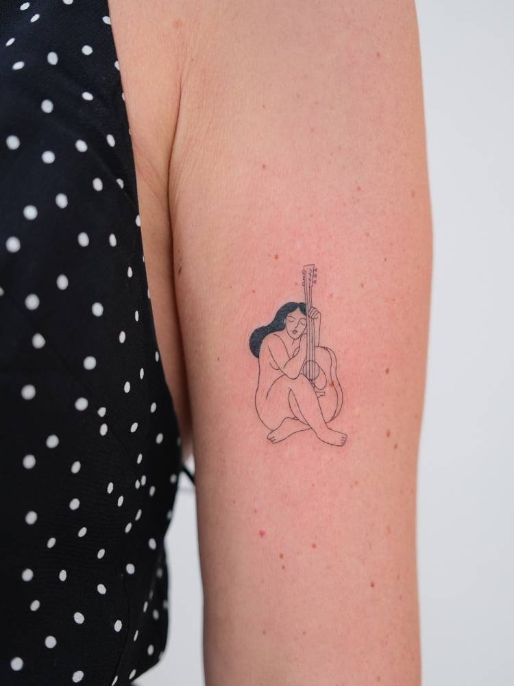 Nude woman and guitar tattooed on the upper arm, fine line style.