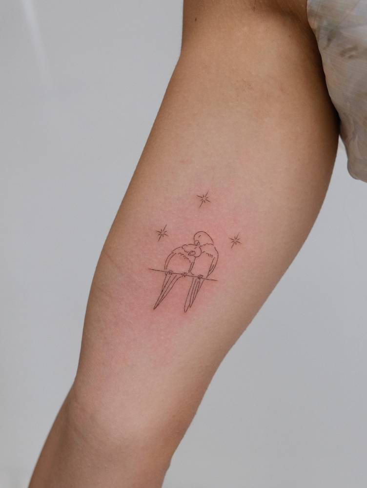 Little lovebirds tattoo in fine line style located on the inner arm.