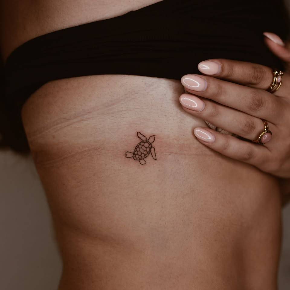 Tiny minimalistic turtle tattoo located on the rib.