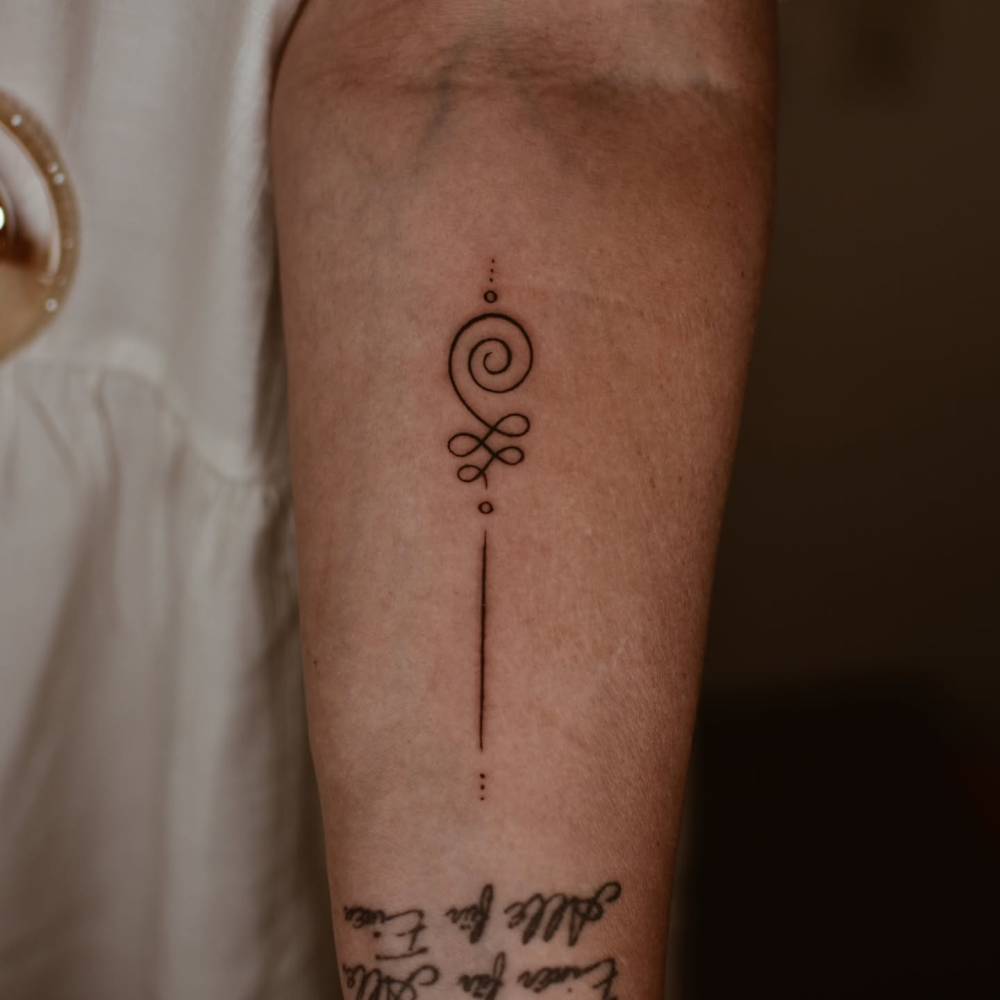 Line art style unalome tattoo located on the inner forearm.