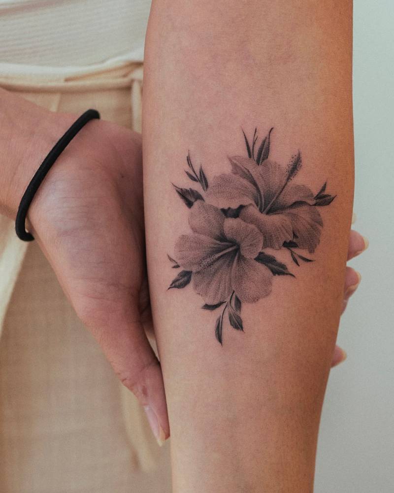 Hibiscus flowers tattooed on the inner forearm, micro-realistic style.