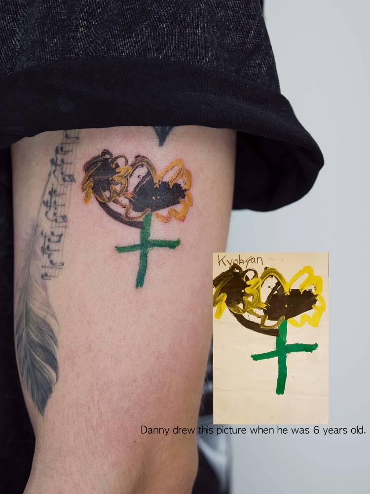 Child's drawing tattooed on the upper arm, done in watercolor style.