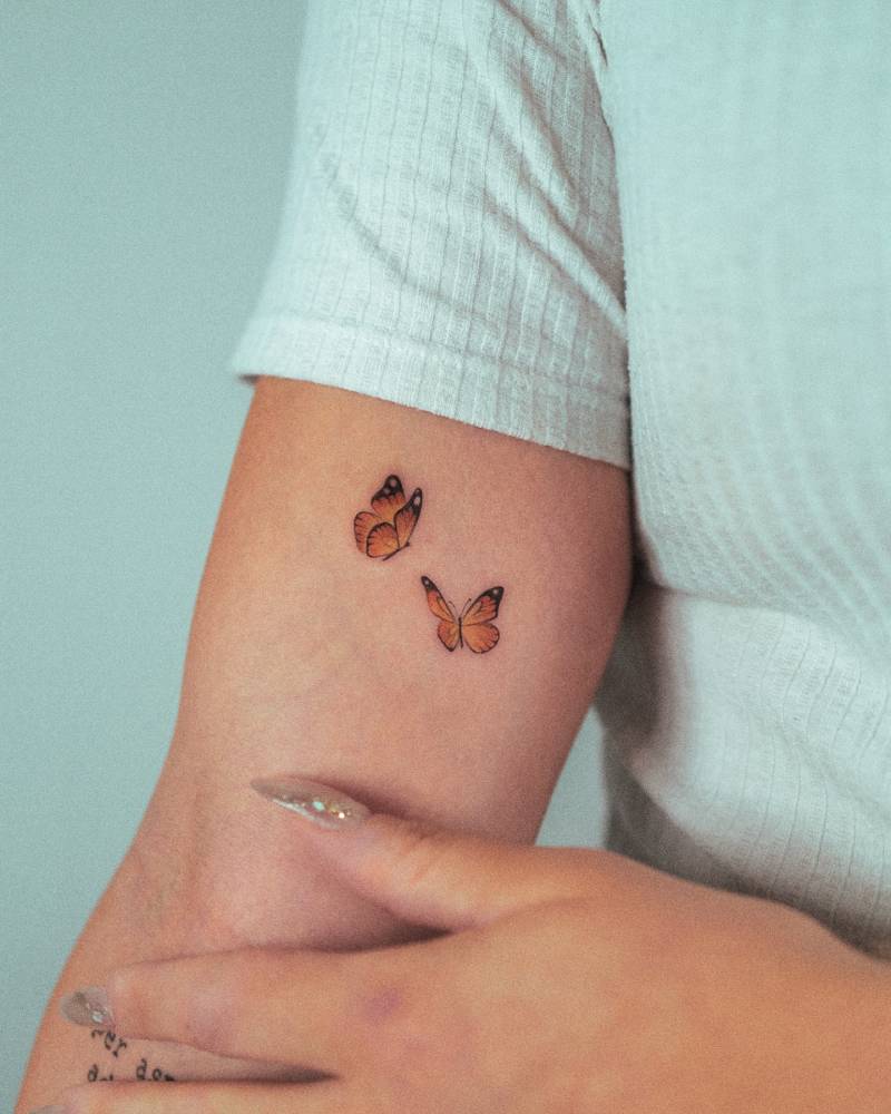 Orange butterfly couple tattooed on the inner arm, done in micro-realistic style.