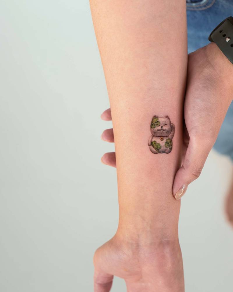 Little maneki-neko tattoo in micro-realistic style placed on the wrist.