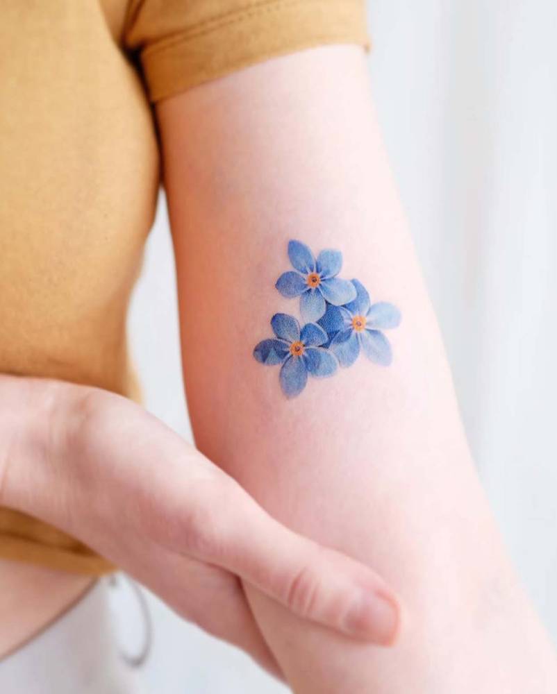 Forget-me-not flowers tattooed on the inner arm, done in micro-realistic style.