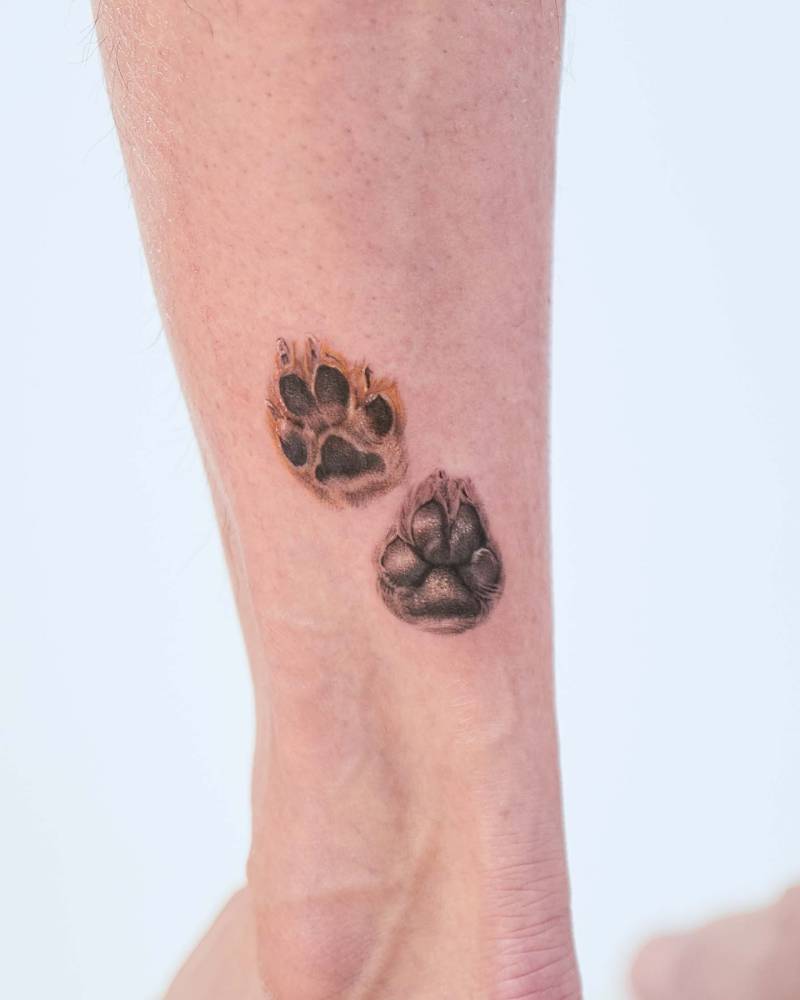 Dog paws tattooed on the achilles, done in micro-realistic style.