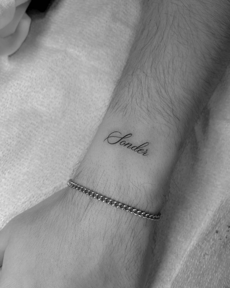 Word "sonder" lettering tattoo placed on the wrist.