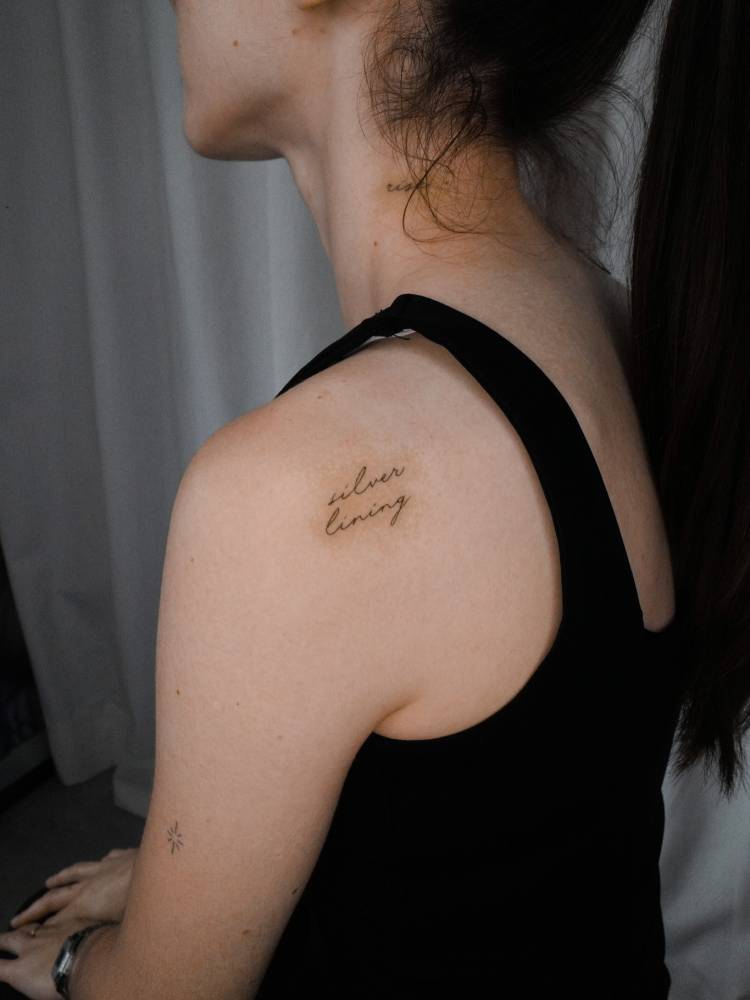 Handwritten font "silver lining" tattoo located on the shoulder blade.