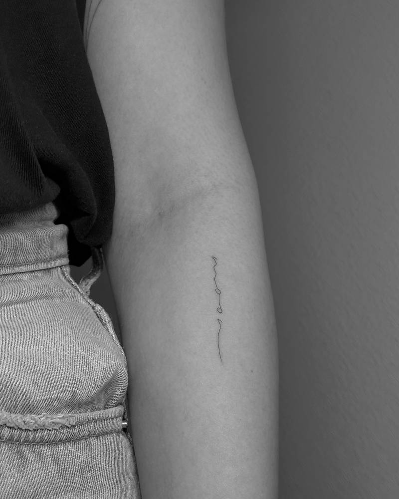 Handwritten lettering tattoo of the word "moon" located on the forearm.