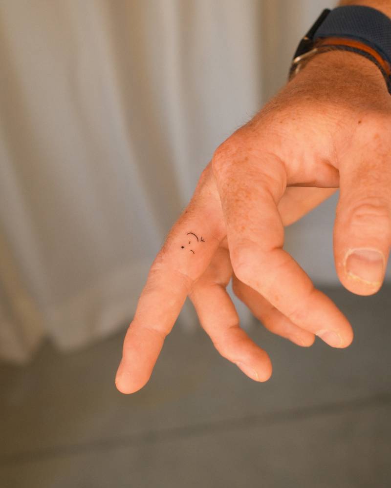 Wink tattoo in minimalistic style located on the finger.