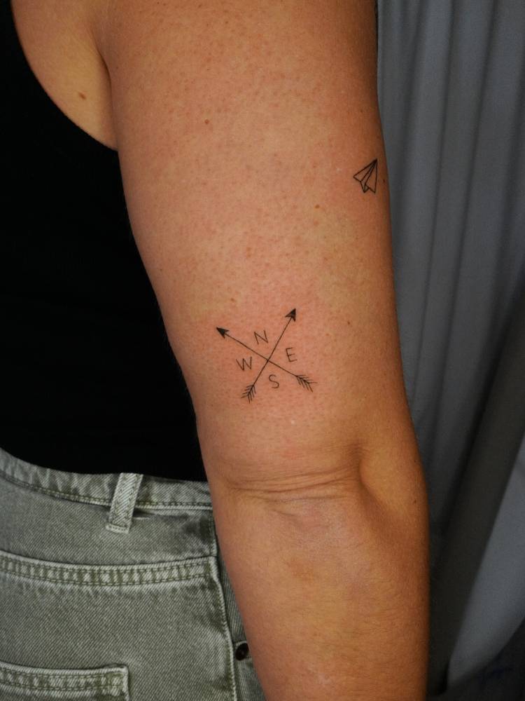 Crossed arrows and compass rose tattoo located on the tricep.