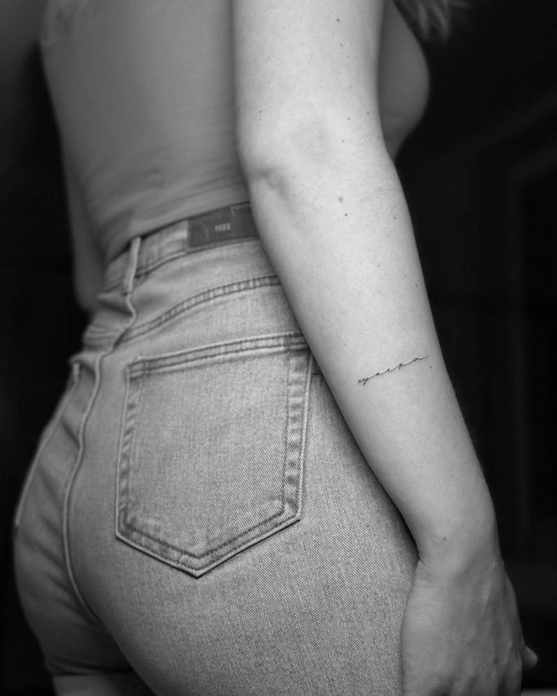 Russian word in handwritten font tattooed on the forearm.
