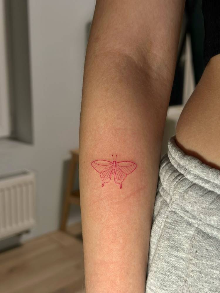 Red butterfly tattoo in fine line style done on the forearm.