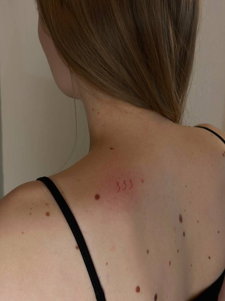 Angel number "333" in red ink tattooed on the shoulder blade.
