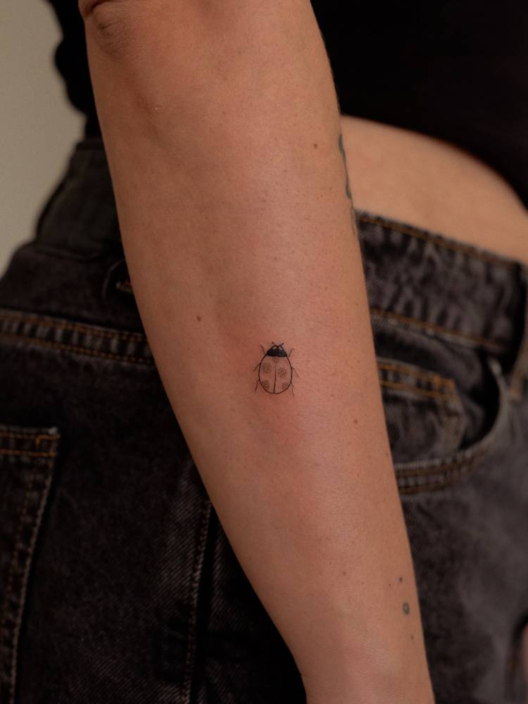 Minimalistic style ladybug tattoo located on the forearm.