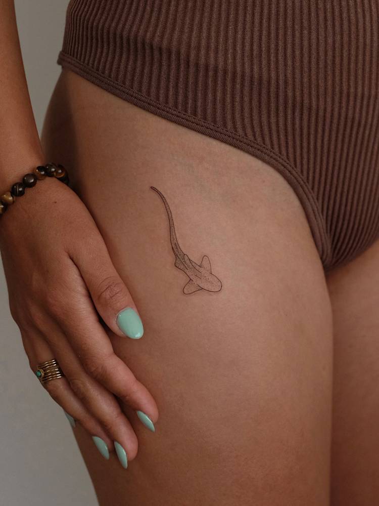 Leopard shark tattooed on the thigh, fine line style.