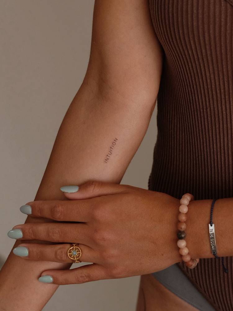 Handwritten font word "intuition" tattoo done on the inner forearm.