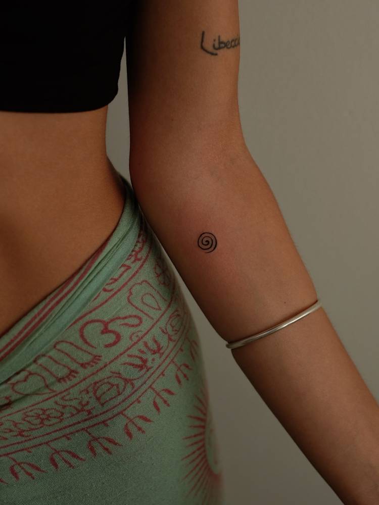 Tiny minimalistic spiral tattooed on the inner forearm.