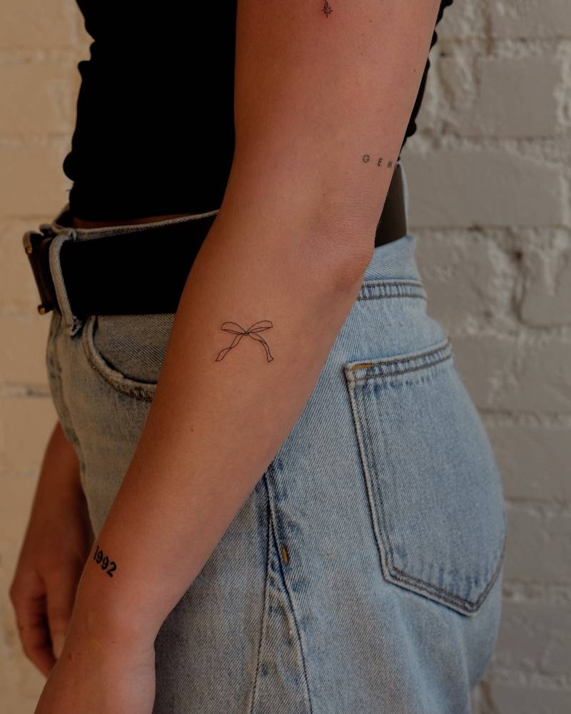 Bow tattoo in fine line style placed on the forearm.