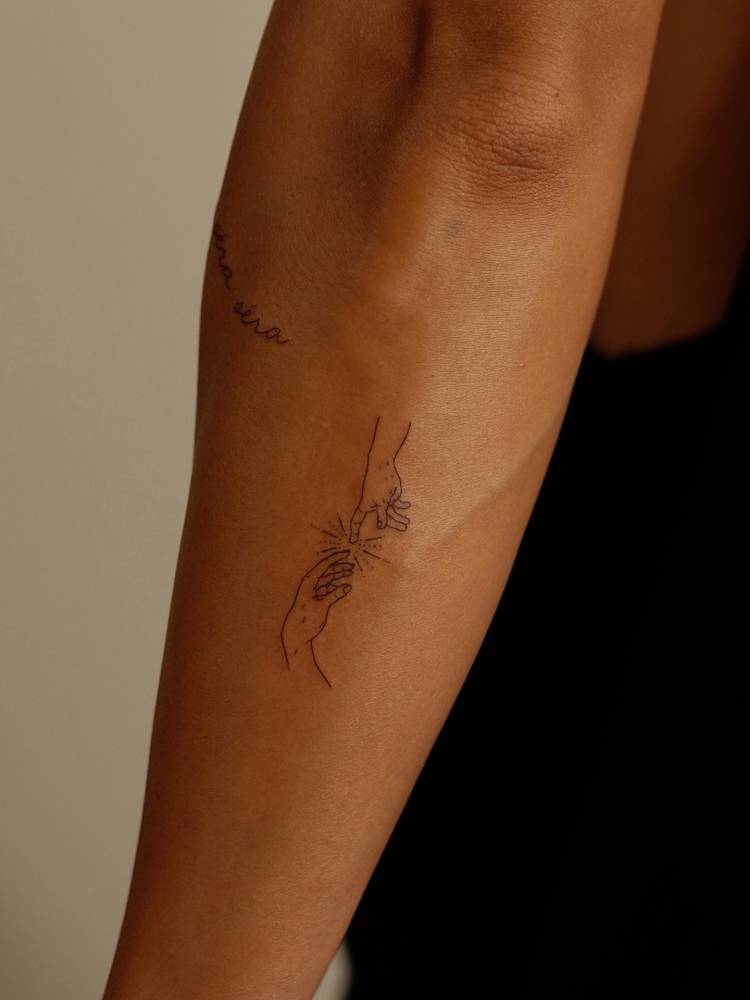 'Creation of Adam' hands tattooed on the forearm, minimalistic style.