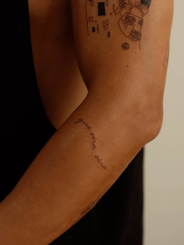 "Que será, será" lettering tattoo handwritten on the forearm.