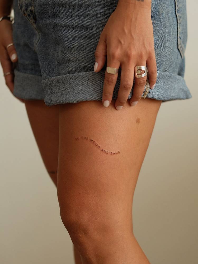 "To the moon and back" lettering tattoo done on the thigh.
