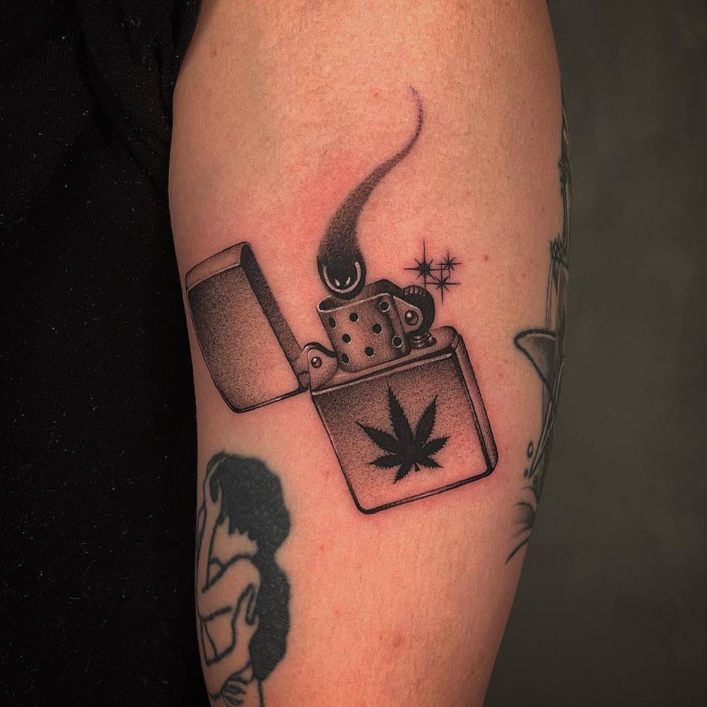 Dotwork style lighter and marijuana leaf tattoo located on the upper arm.