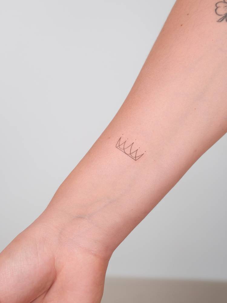 Fine line style crown tattoo located on the wrist.