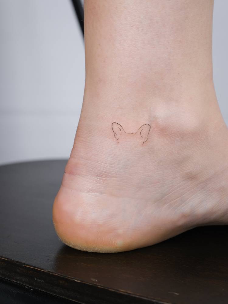 Tiny dog ears tattoo in minimalistic style placed on the ankle.