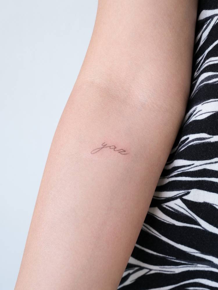 Handwritten lettering tattoo of the name "Yaz" located on the inner forearm.