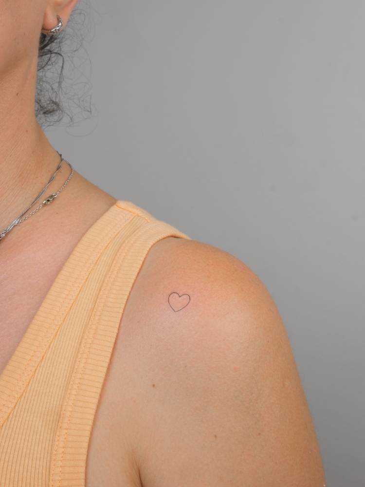 Tiny minimalistic heart tattoo placed on the shoulder.