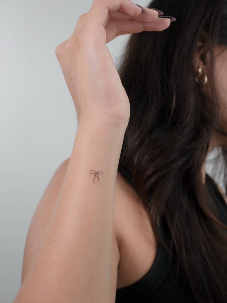 Micro bow tattoo located on the wrist, done in minimalistic style.
