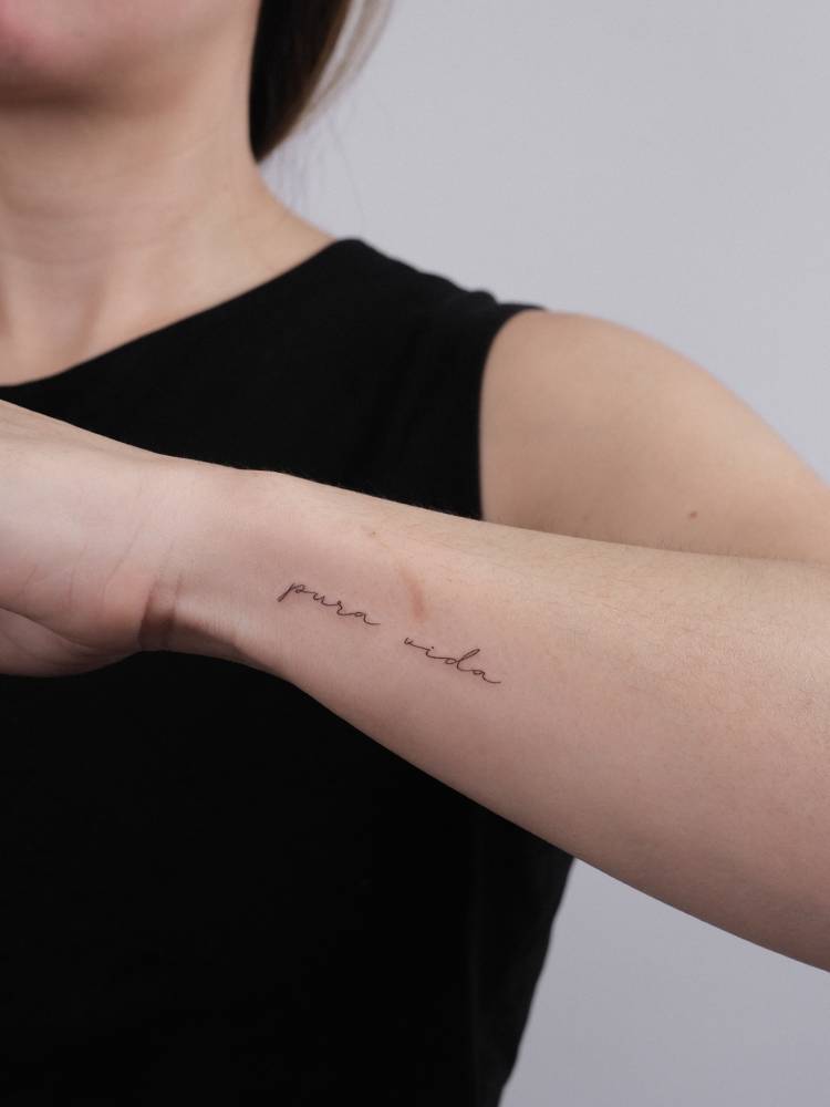 Lettering tattoo that says "pura vida" handwritten on the wrist.