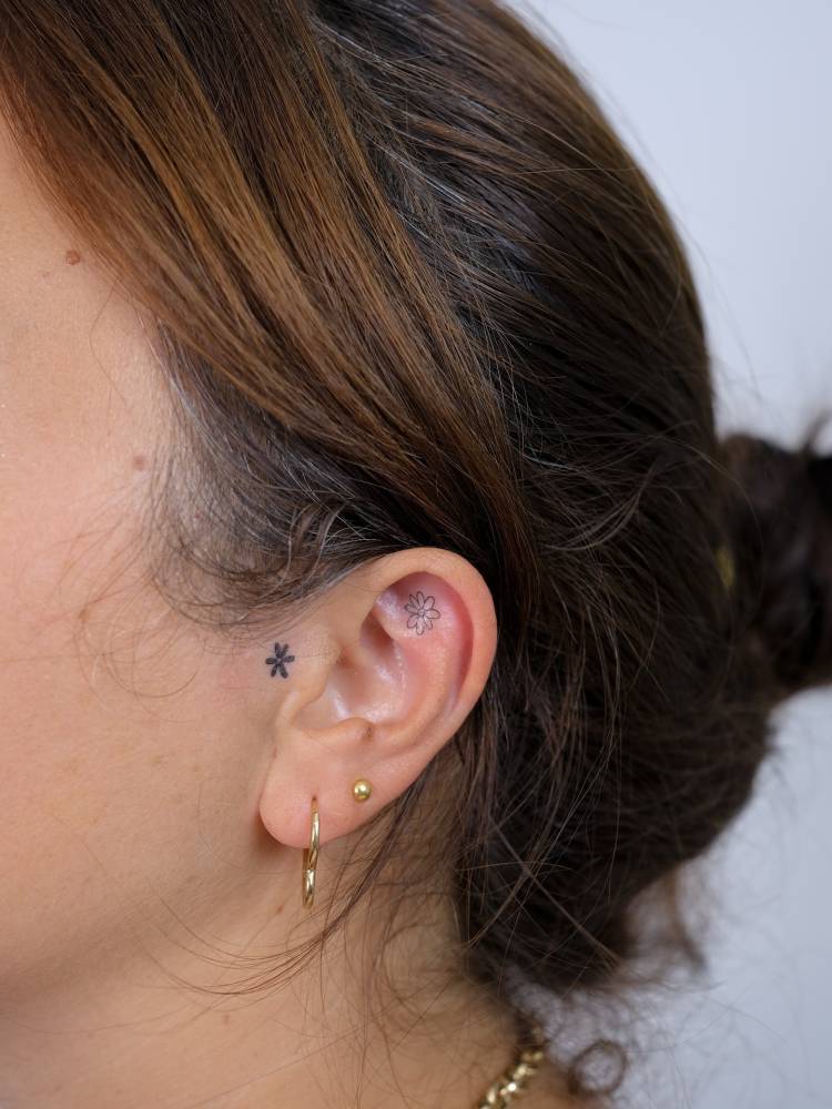 Tiny fine line flower tattoo located on the ear.