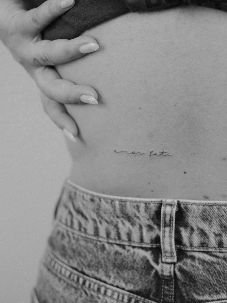 "Amor fati" lettering tattoo located on the lower back.