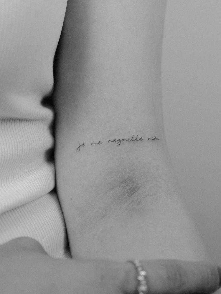 "Je ne regrette rien" lettering tattoo placed on the bicep.