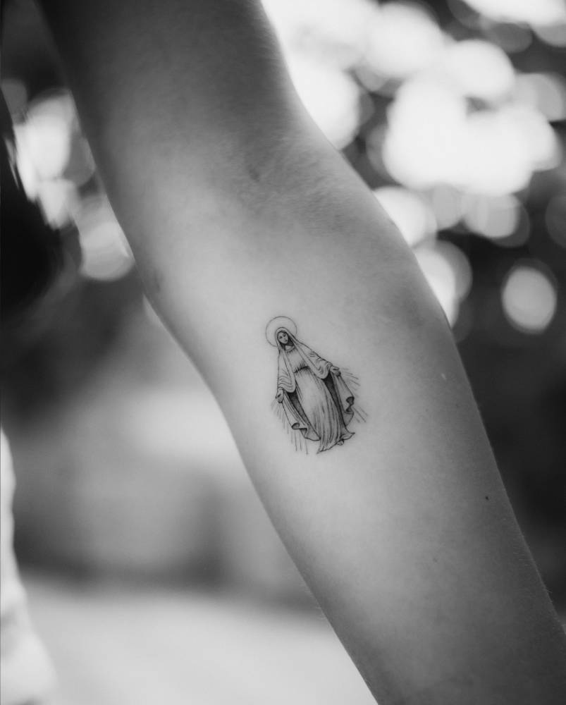 Virgin Mary tattoo in illustrative style located on the inner forearm.